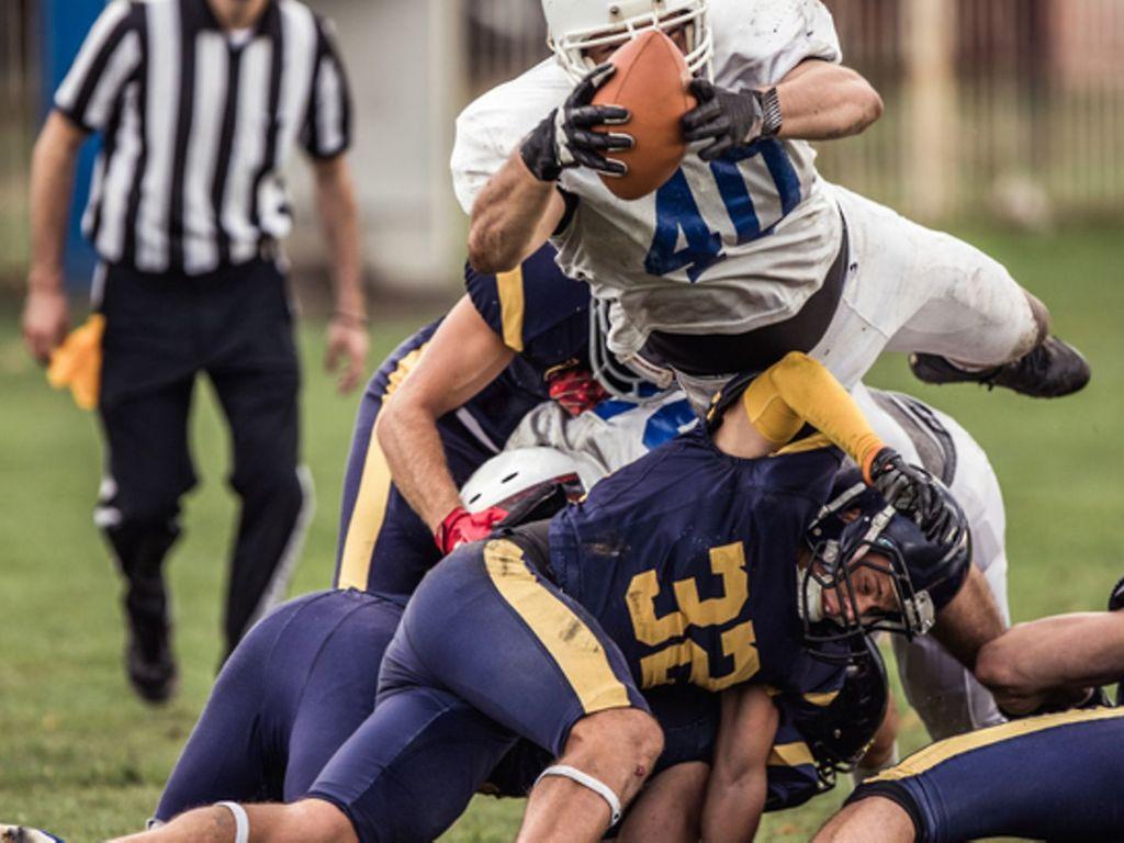 American Football: Mehrere Football-Spieler in voller Montur fallen bei einem Spiel übereinander her.