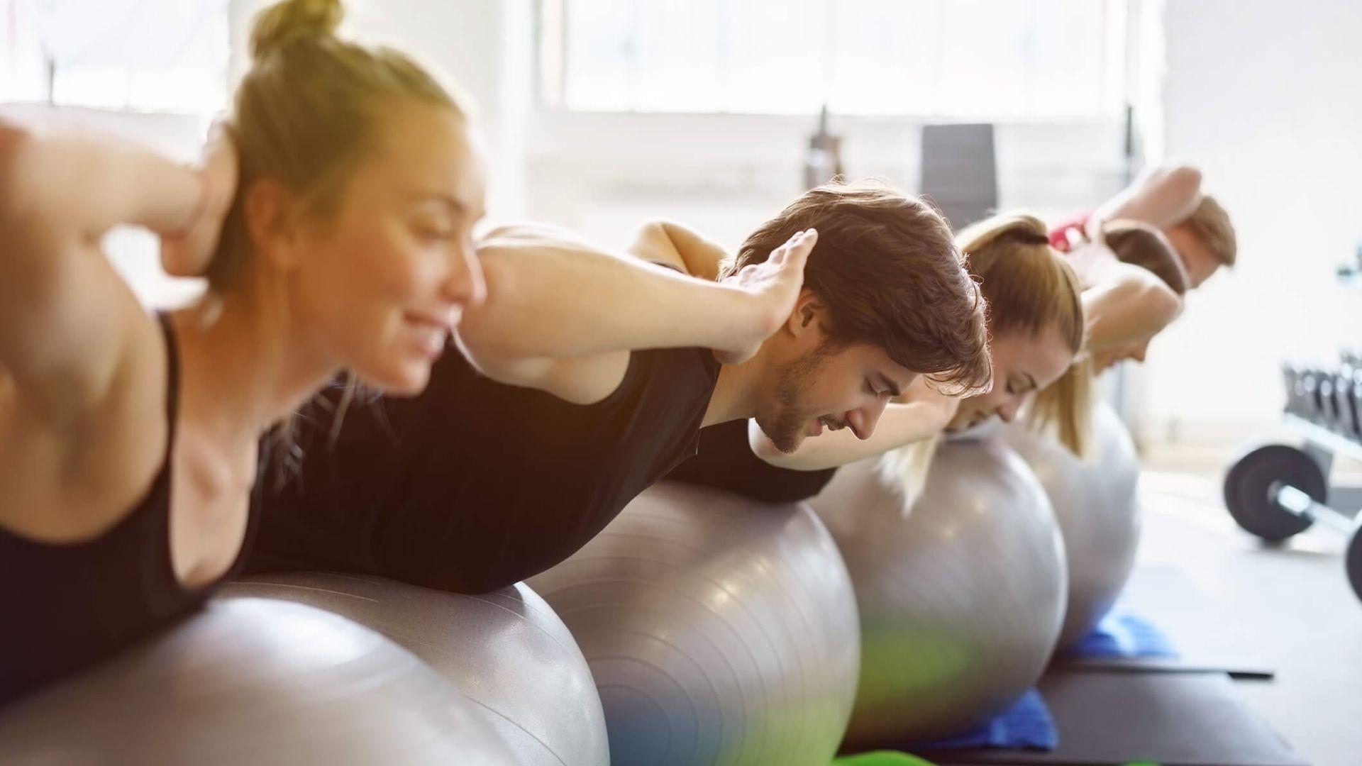 Sportmythen: Eine Gruppe junger Menschen macht Rückenübungen auf Gymnastikbällen,