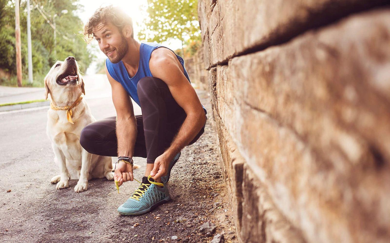 Hitze-Training Schwitzender Mann mit Hund macht sich die Laufschuhe wieder zu.