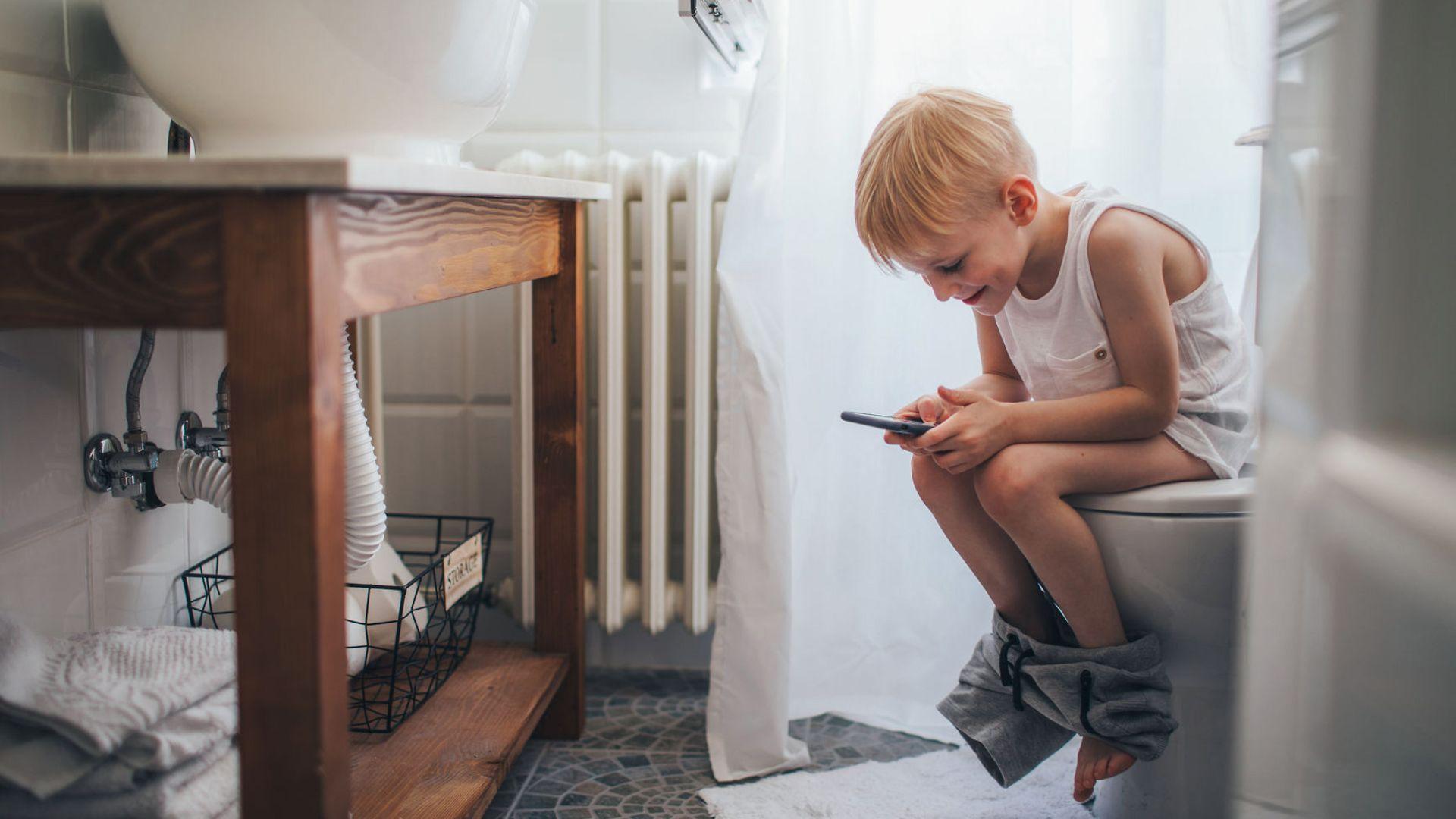 Verdauung und Darmerkrankungen: Junge mit Handy sitzt auf Toilette.