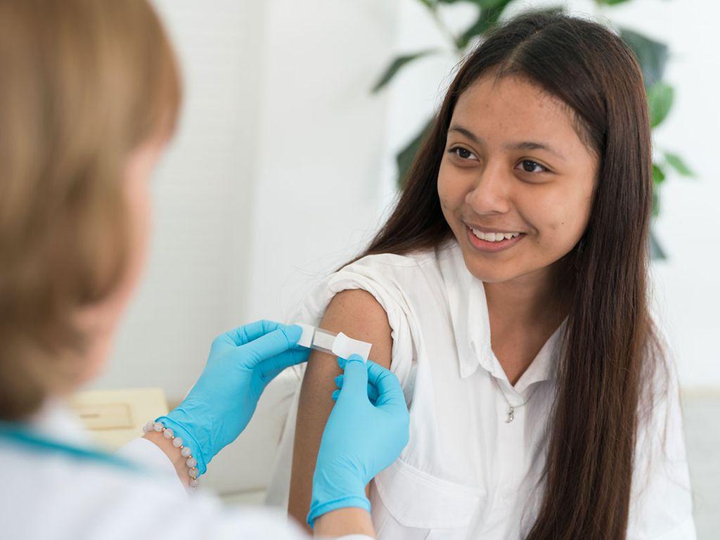 HPV-Impfung: Ärztin klebt einer Teenagerin nach der Impfung ein Pflaster auf den Arm. 