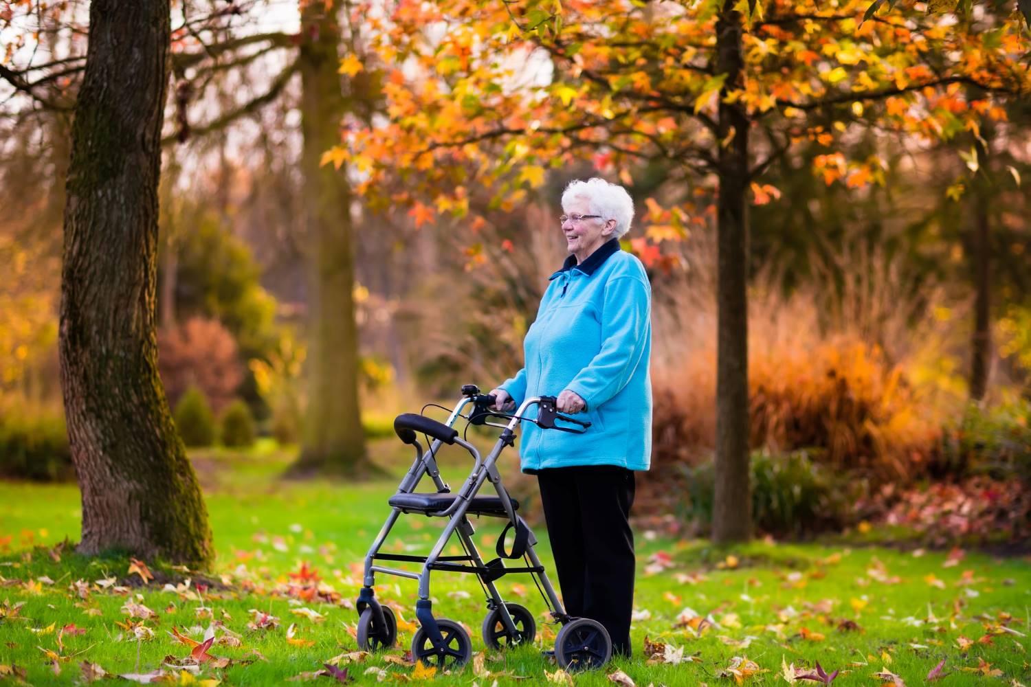 Rollatoren: Ältere Frau steht mit ihrem Rollator auf einer herbstlichen Wiese.