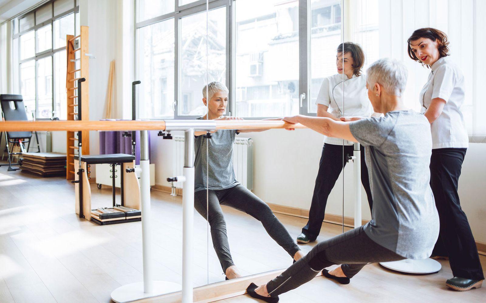 Rehasport: Frau und Trainerin an Stange am Spiegel.