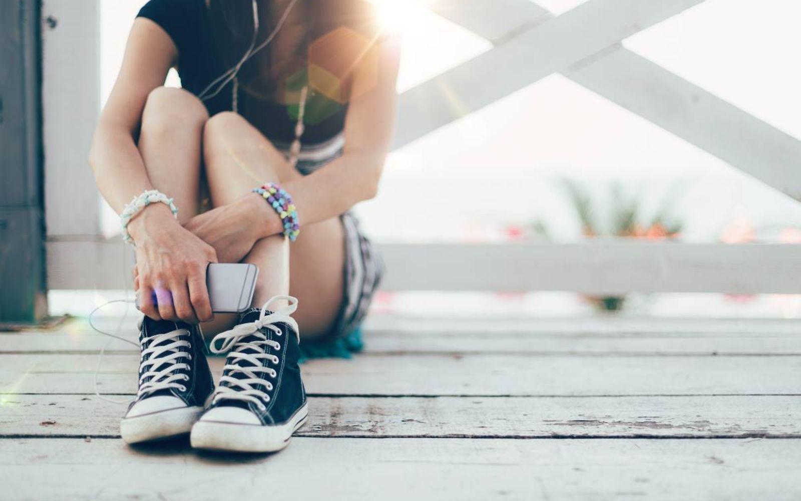 veo: Mädchen mit Smartphone sitzt draußen auf dem Boden