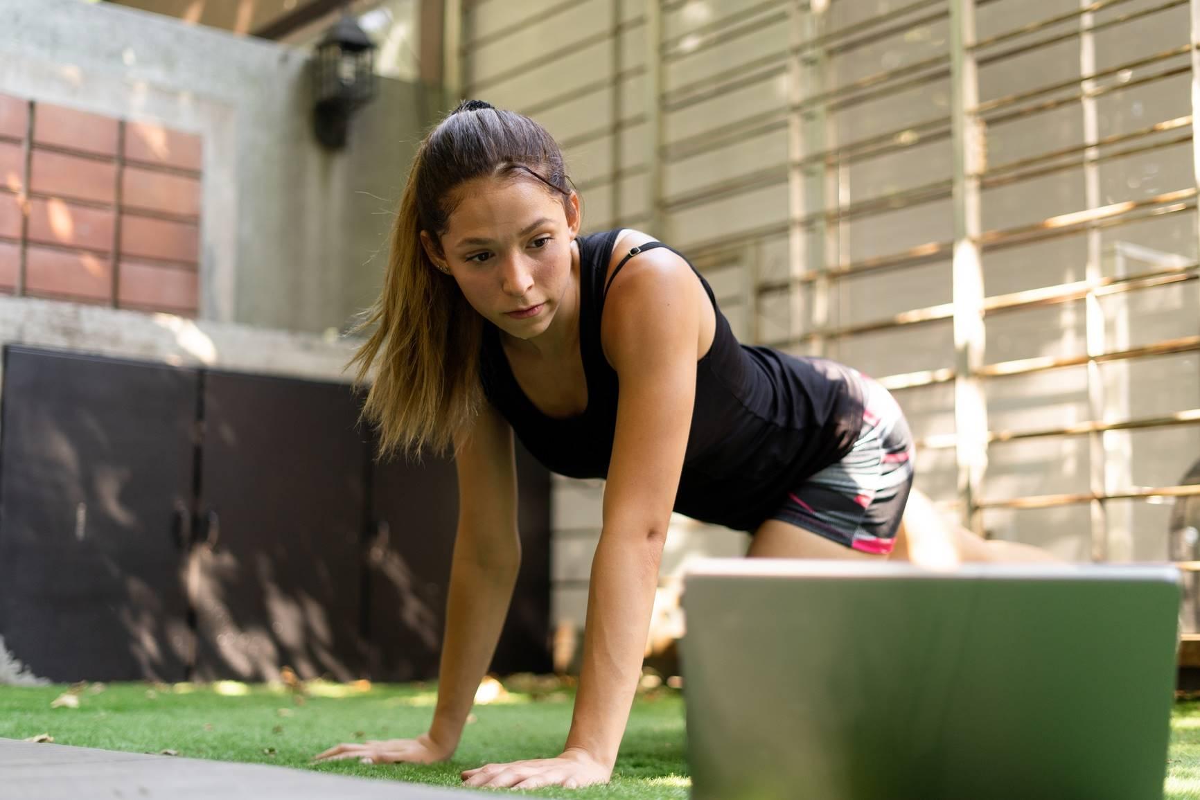 Online-Coachings: Junge Frau macht Sport und schaut dabei auf einen Laptop.