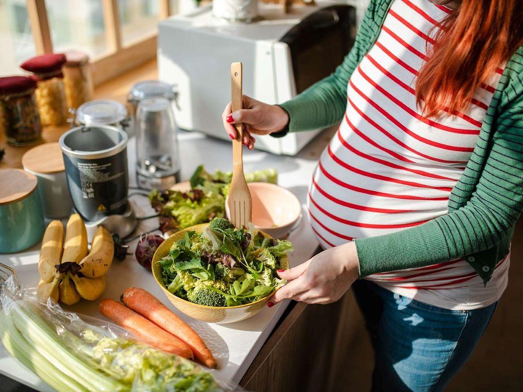 Schwangere Frau bereitet Salat in der Küche zu