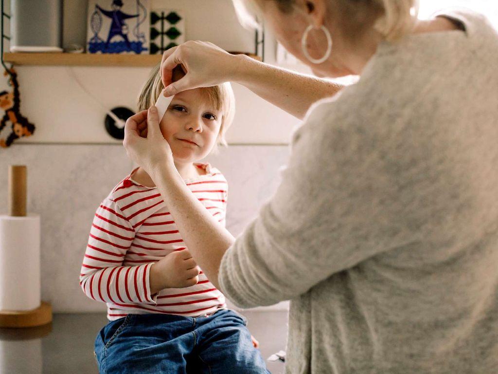 Erste Hilfe am Kind: Mutter klebt Pflaster auf die Schläfe ihres Kindes