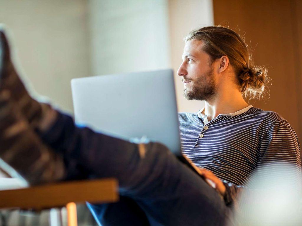 Work-Live-Balance: Mann sitzt in entspannter Pose mit Laptop auf dem Schoß