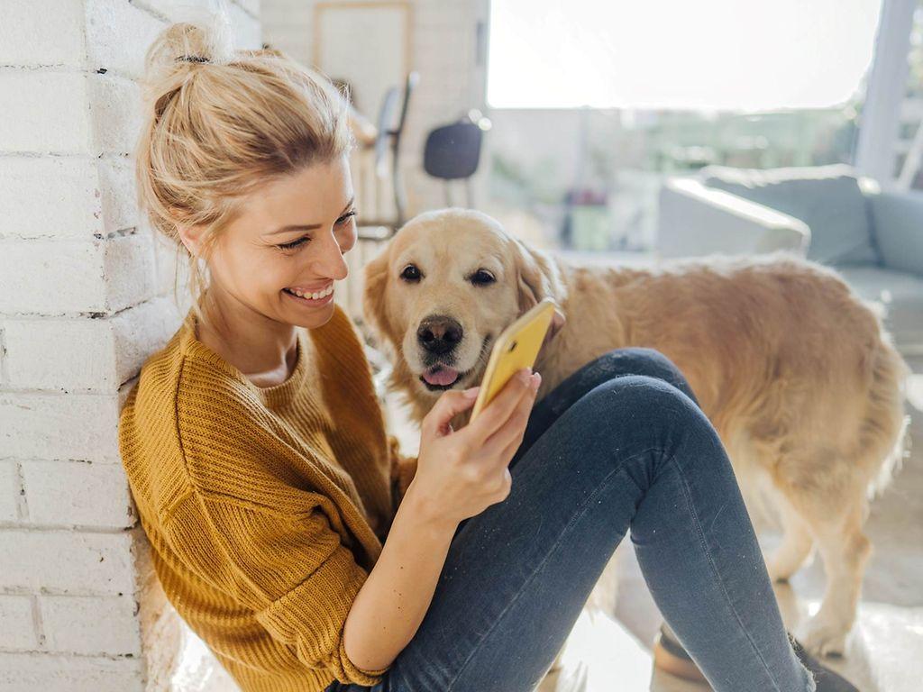 DAK Gesundheit PLUS-Leistungen: Glückliche Frau mit Hund schaut auf Handy.
