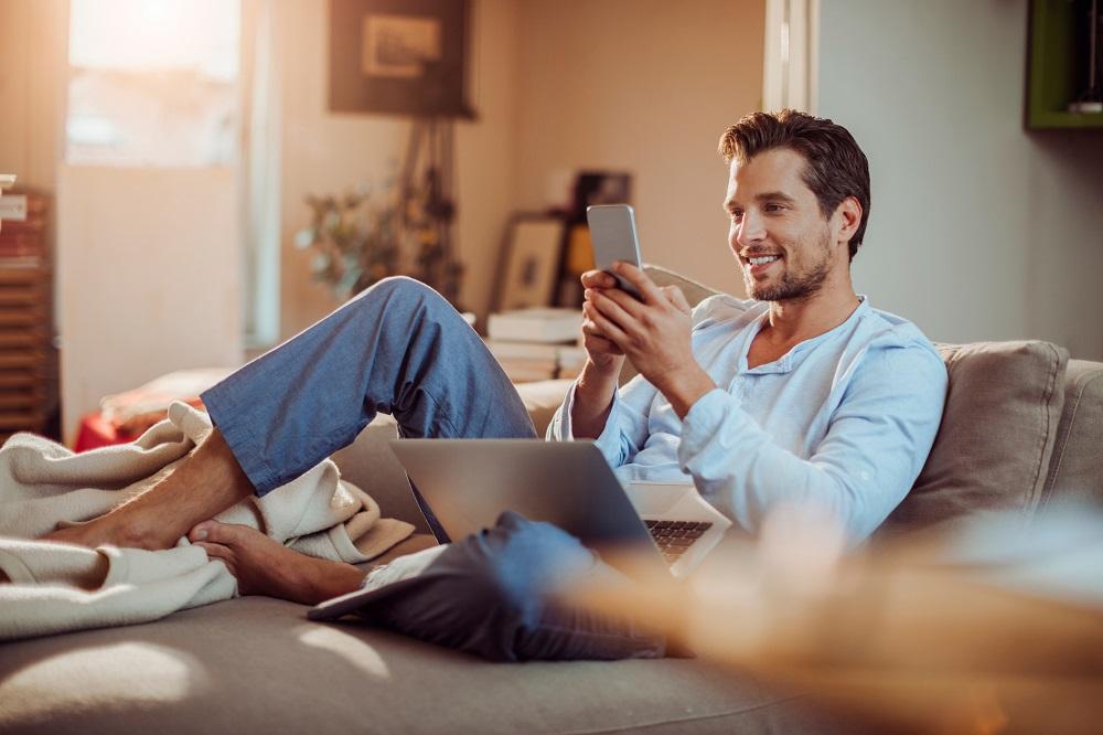 Mann mittleren Alters sitzt entspannt auf einem Sofa und schaut auf sein Smartphone.