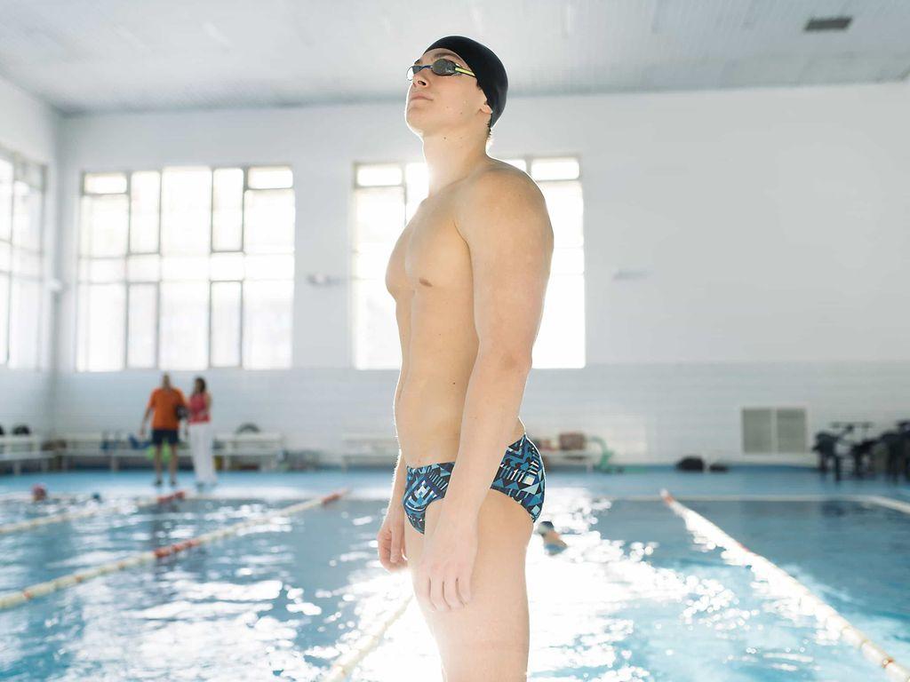 Impotenz: Jüngerer Mann in Badehose, mit Schwimmbrille und Badekappe steht vor einem Schwimmbecken.