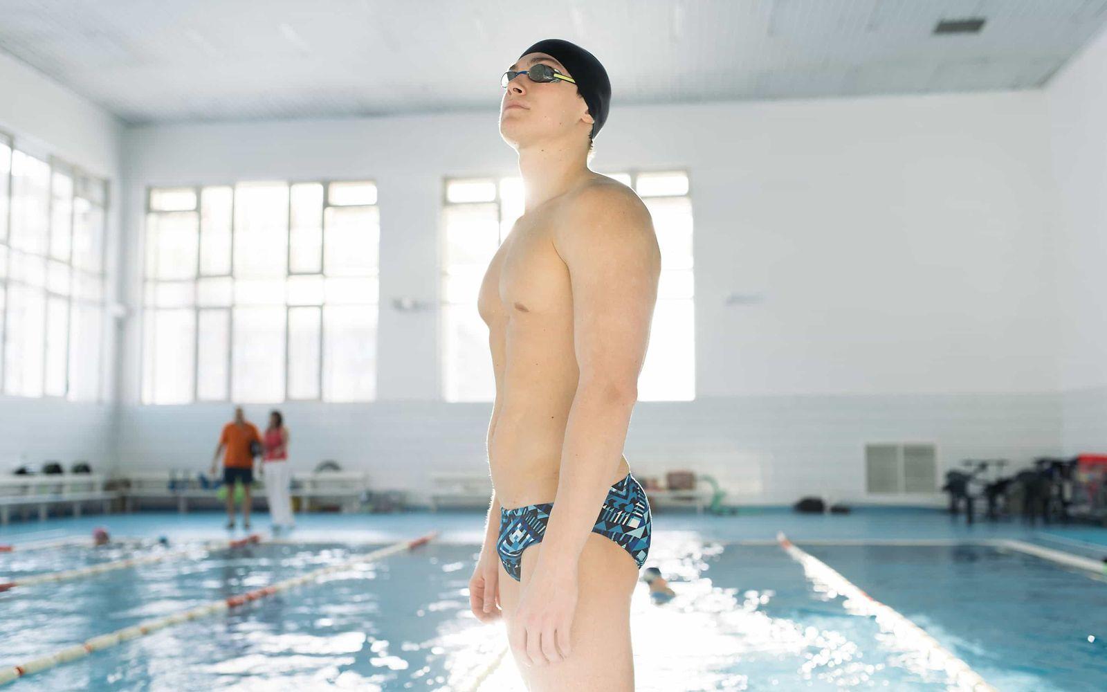 Impotenz: Jüngerer Mann in Badehose, mit Schwimmbrille und Badekappe steht vor einem Schwimmbecken.