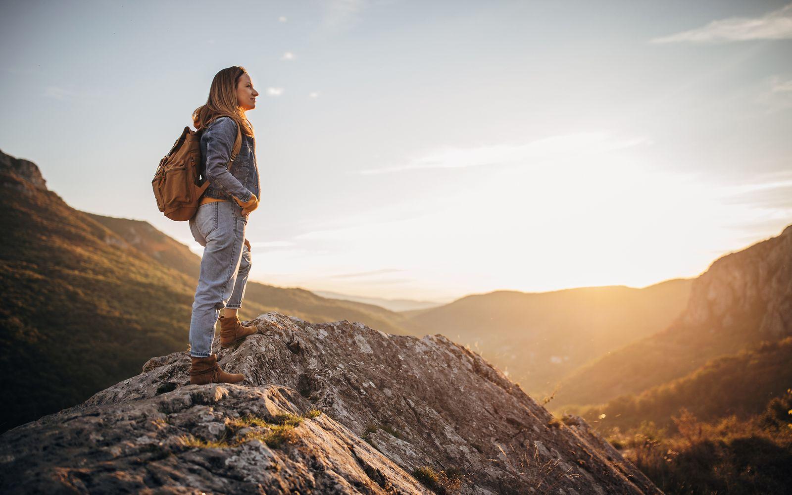 Bild: Junge Frau mit Rucksack steht auf einem Bergipfel und betrachtet das malerische Bergpanorama.