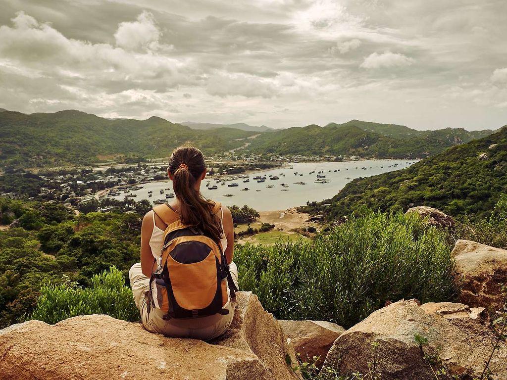 Frau sitzt auf einem Berg und schaut runter auf eine Bucht.