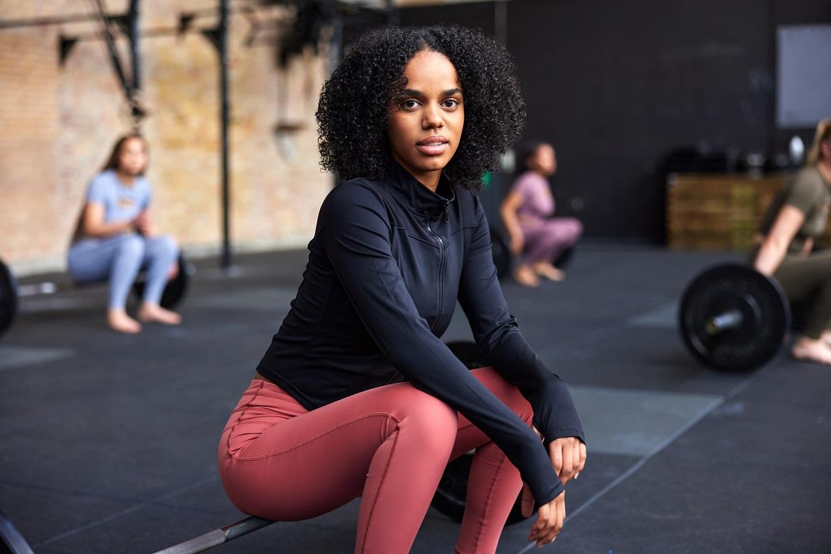 Sportliche junge Frau sitzt auf einer Langhantel in einem Fitnessstudio