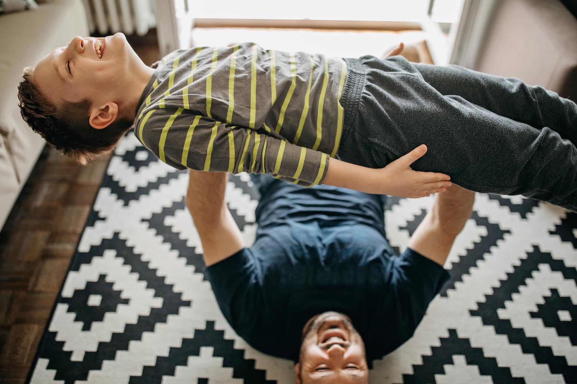 Familienversicherung: Liegender Mann hält Jungen hoch.