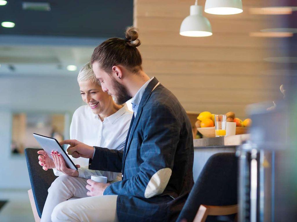 Patientenschulung Ernährung: Ältere Frau und junger Mann nutzen digitales Tablet in einem Seminarraum.