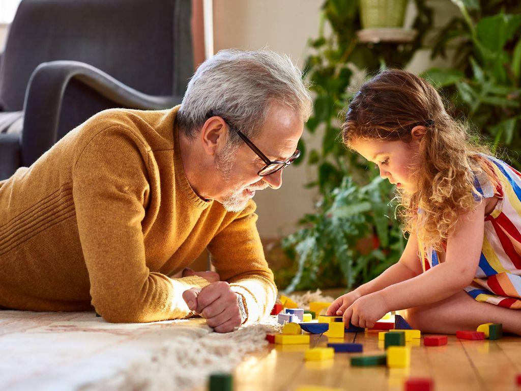 Kinder und Spielzeug: Opa und Enkelin spielen auf dem Boden mit Bauklötzen