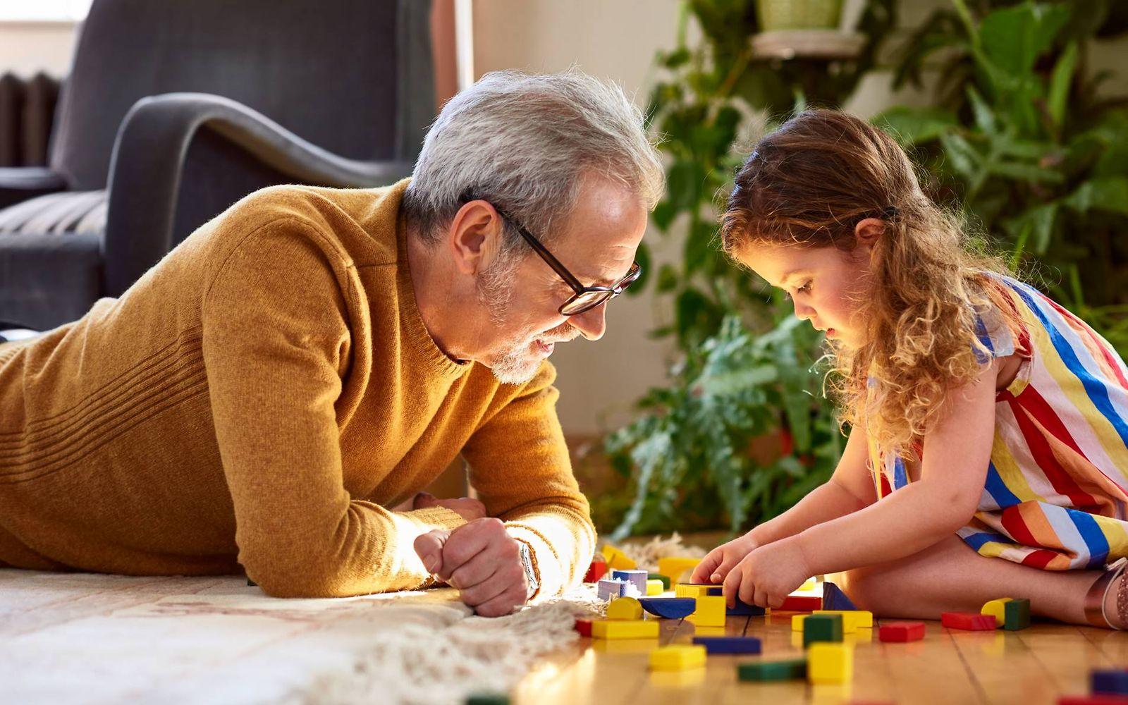 Kinder und Spielzeug: Opa und Enkelin spielen auf dem Boden mit Bauklötzen