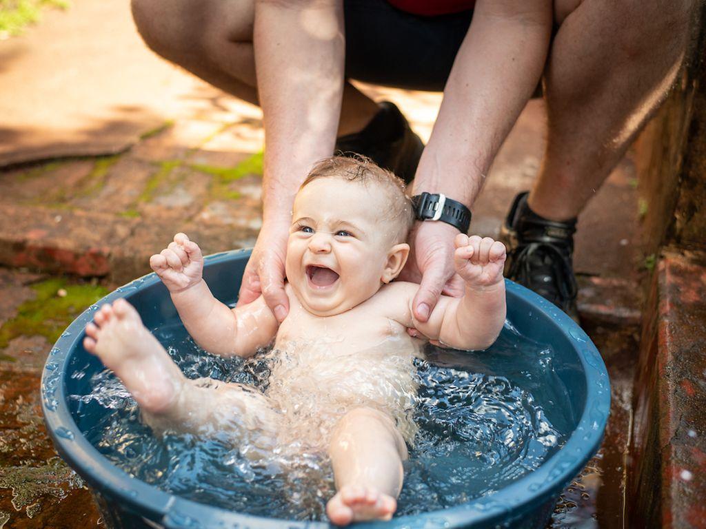 Babys und Hitze: Vater badet sein Baby draußen in einer kleinen Wanne