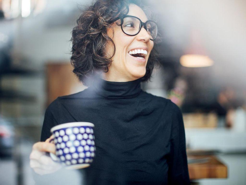 Biologisches Alter: Frau guckt lachend zur Seite und hält eine Tasse in der Hand