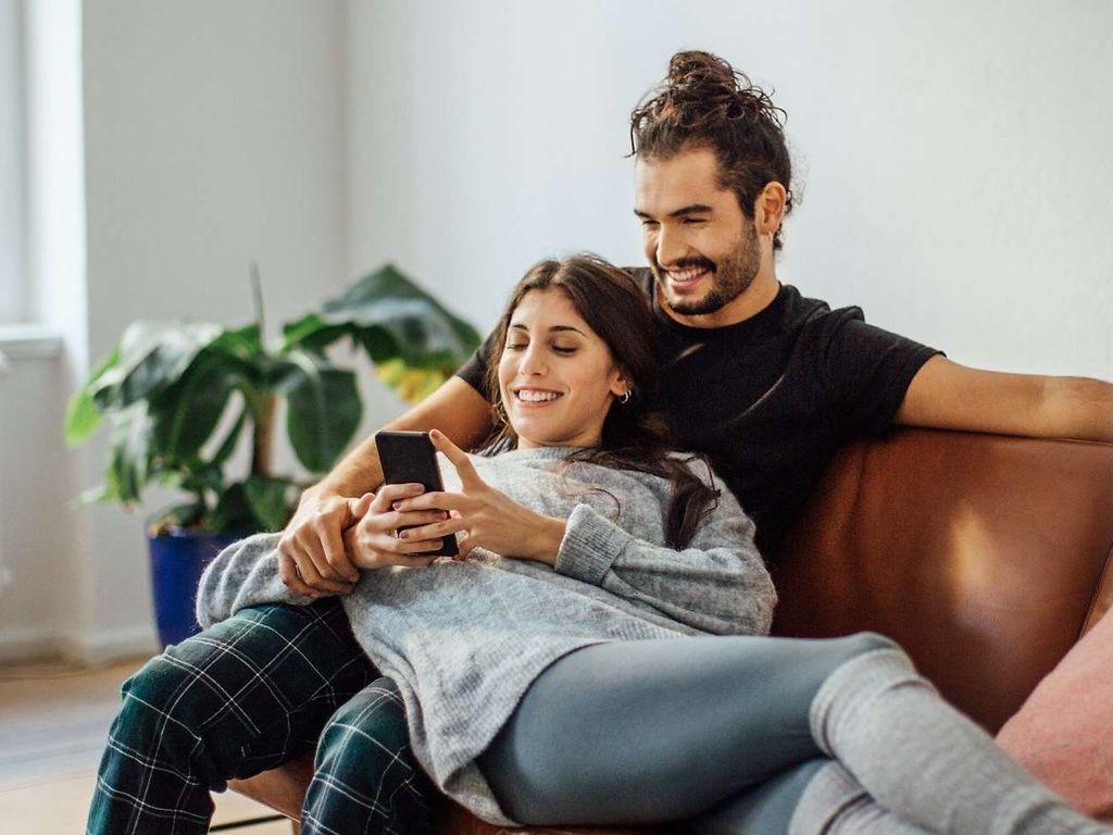 Auszeichnungen für DAK: Junges Paar sitzt auf dem Sofa und schaut gemeinsam auf ein Handy.