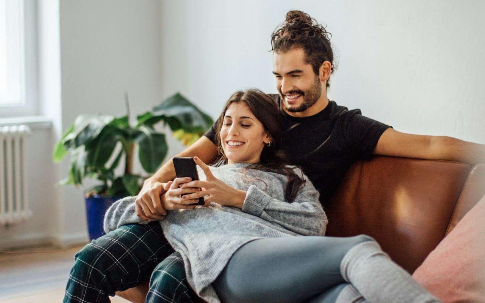 Auszeichnungen für DAK: Junges Paar sitzt auf dem Sofa und schaut gemeinsam auf ein Handy.