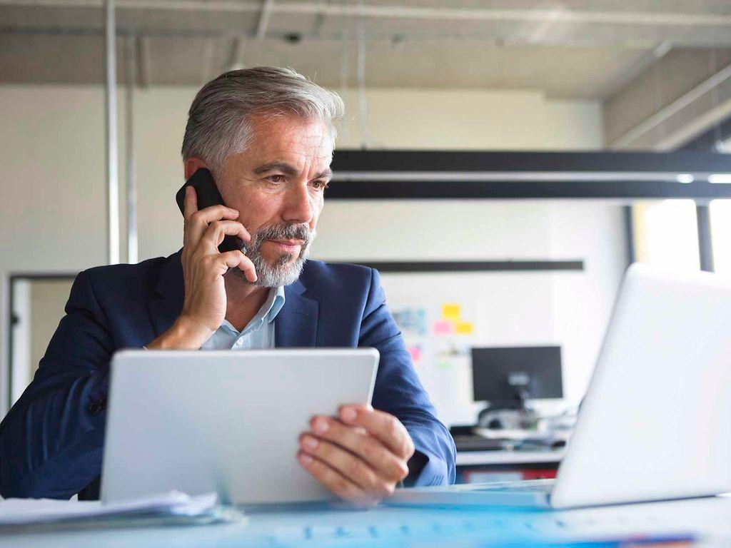 Bild: Älterer Business-Mann telefoniert und schaut auf einen Laptop.