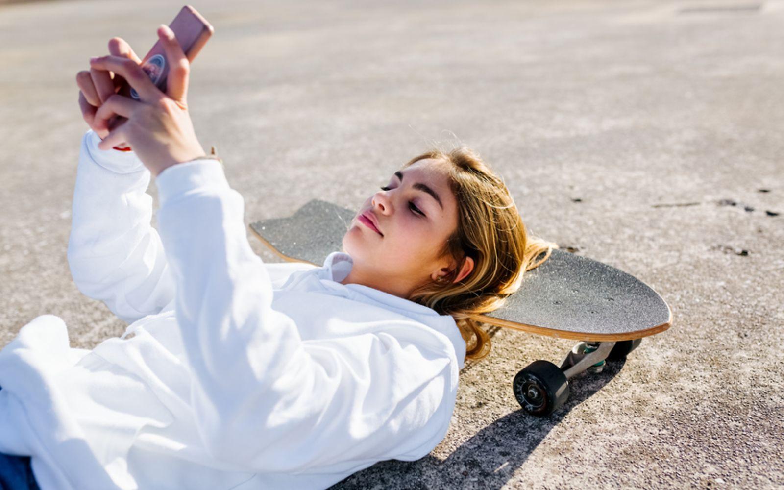 Symbolbild für Schweigepflicht: Ein Teenager-Mädchen macht ein Selfie auf dem Skateboard