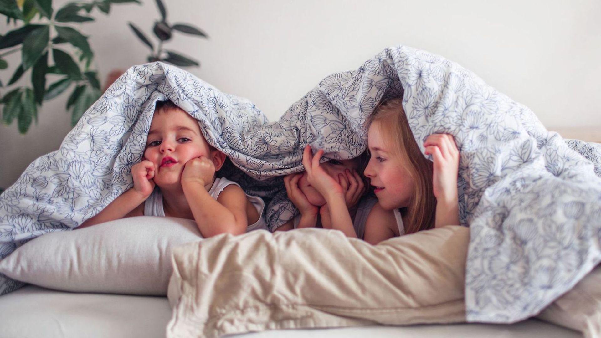 Die leistungsstarke Krankenkasse für Familien: Drei Kinder verstecken sich unter einer Bettdecke.