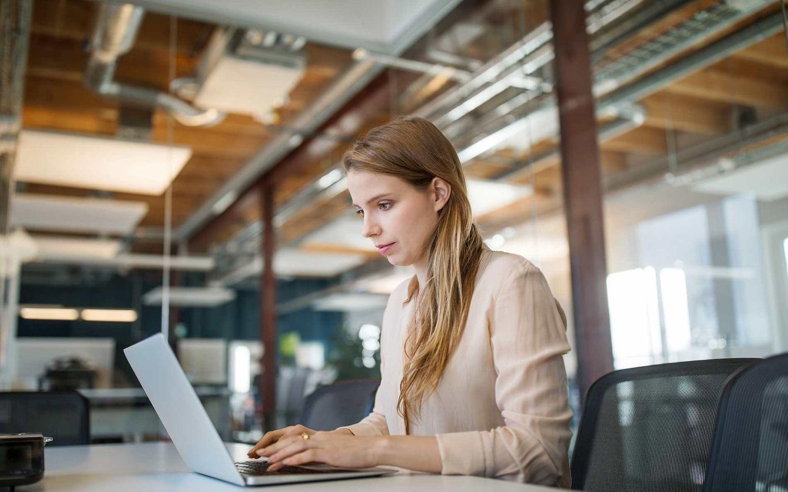 Bild: Junge Frau sitzt im Büro am Laptop und sieht zufrieden aus.