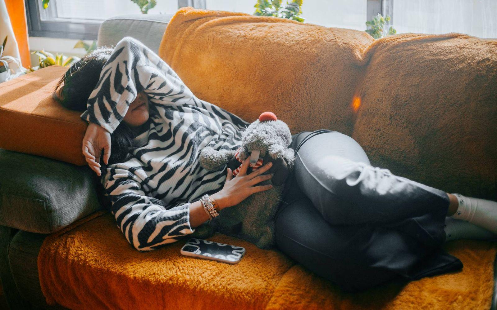 Symbolbild Menstruationsschmerzen: Junge Frau liegt mit Menstruationsschmerzen auf dem Sofa.