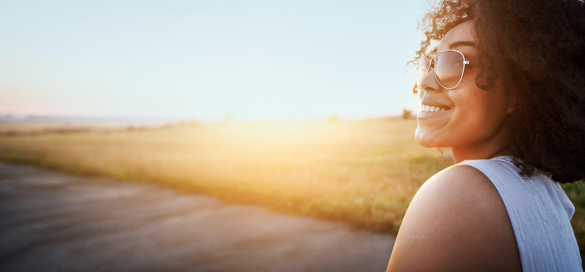 Junge Frau mit Sonnenbrille läuft durch einen Park.