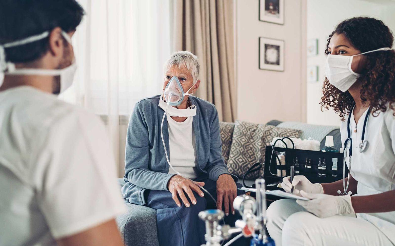 Bild: Ältere Patientin hat eine Atemmaske auf und unterhält sich mit Ärztin und Pfleger