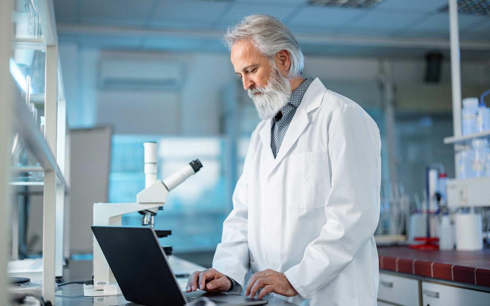 Bild: Chemiker steht im Labor und schaut etwas im Laptop nach.