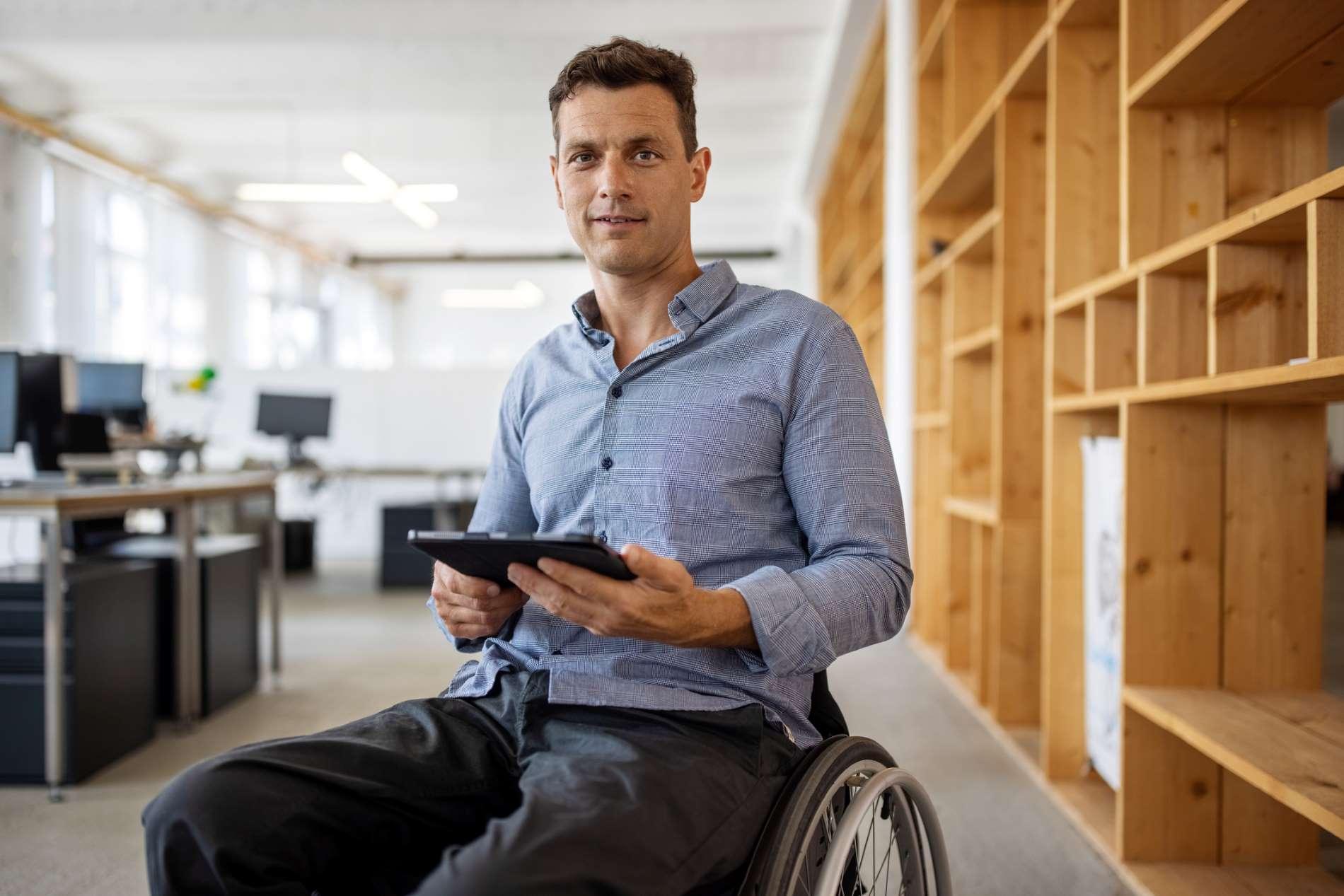 Bild: Mann im Rollstuhl schaut etwas im Büro auf dem Tablet nach