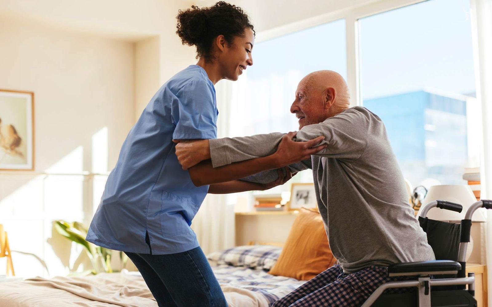 Bild: Pflegerin hilft einem älteren Mann zuhause aus seinem Rollstuhl