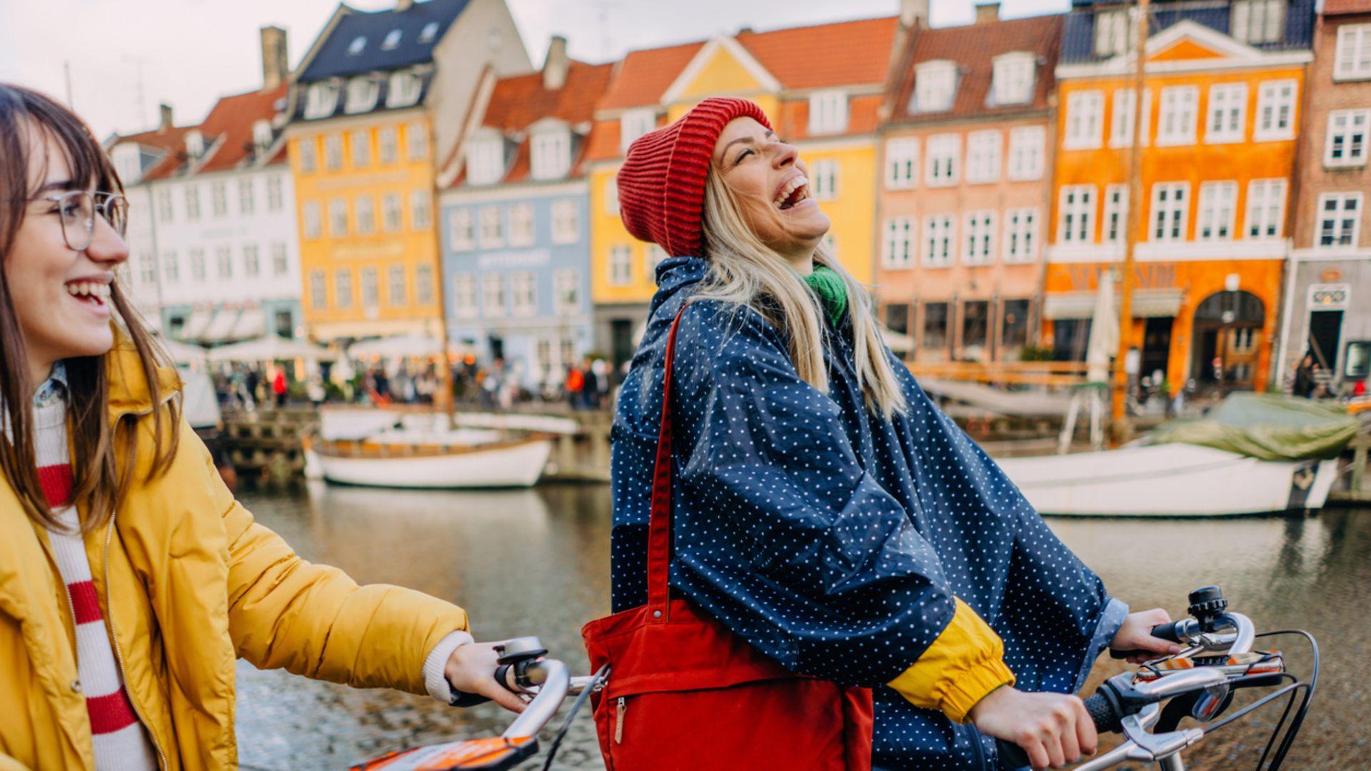 Zwei Frauen fahren lachend mit ihren Rädern durch Kopenhagen.