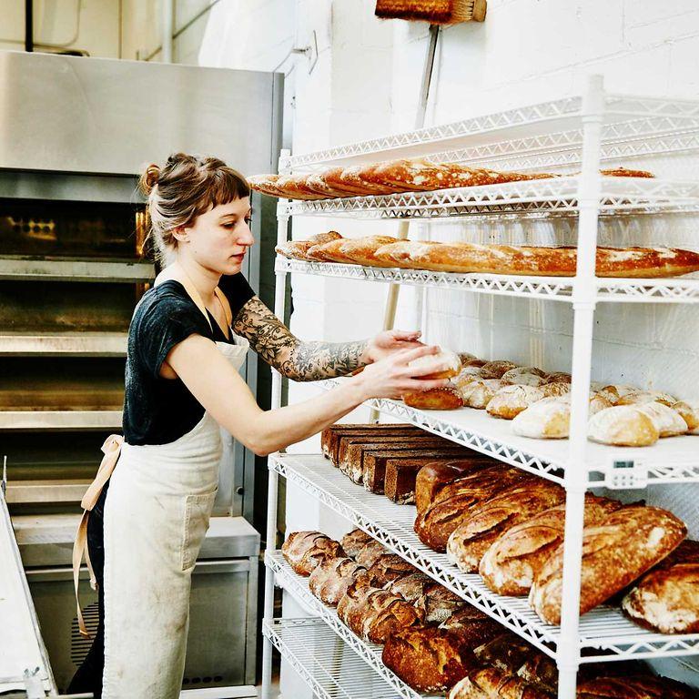 Bild: Mitarbeiterin in einer Bäckerei legt fertiges Brot zum Abkühlen ins Regal.