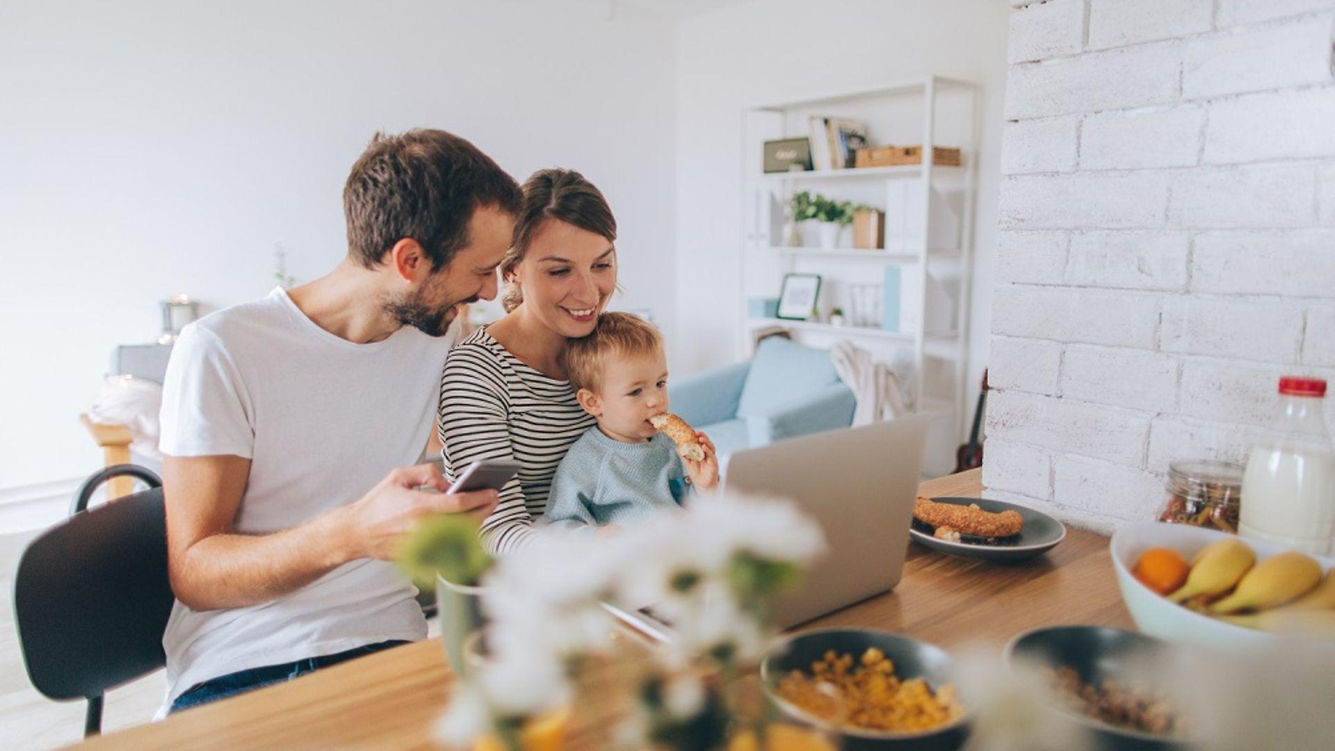 Familie beim Frühstück mit Handy und Laptop.