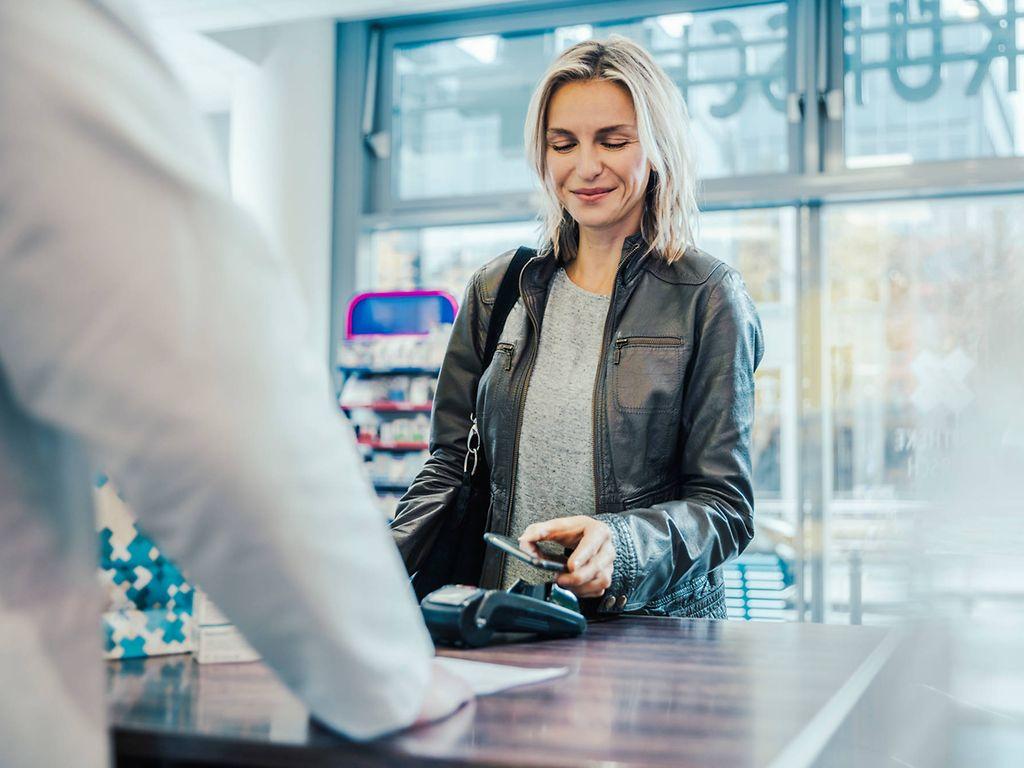 Bild: Frau löst ein Rezept per Handy in der Apotheke ein.