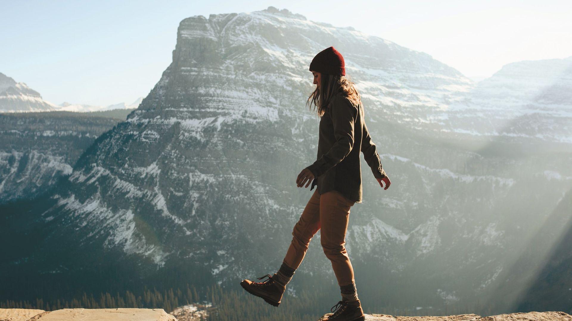 Woman walking on ledge against a beautiful blue mountain range.