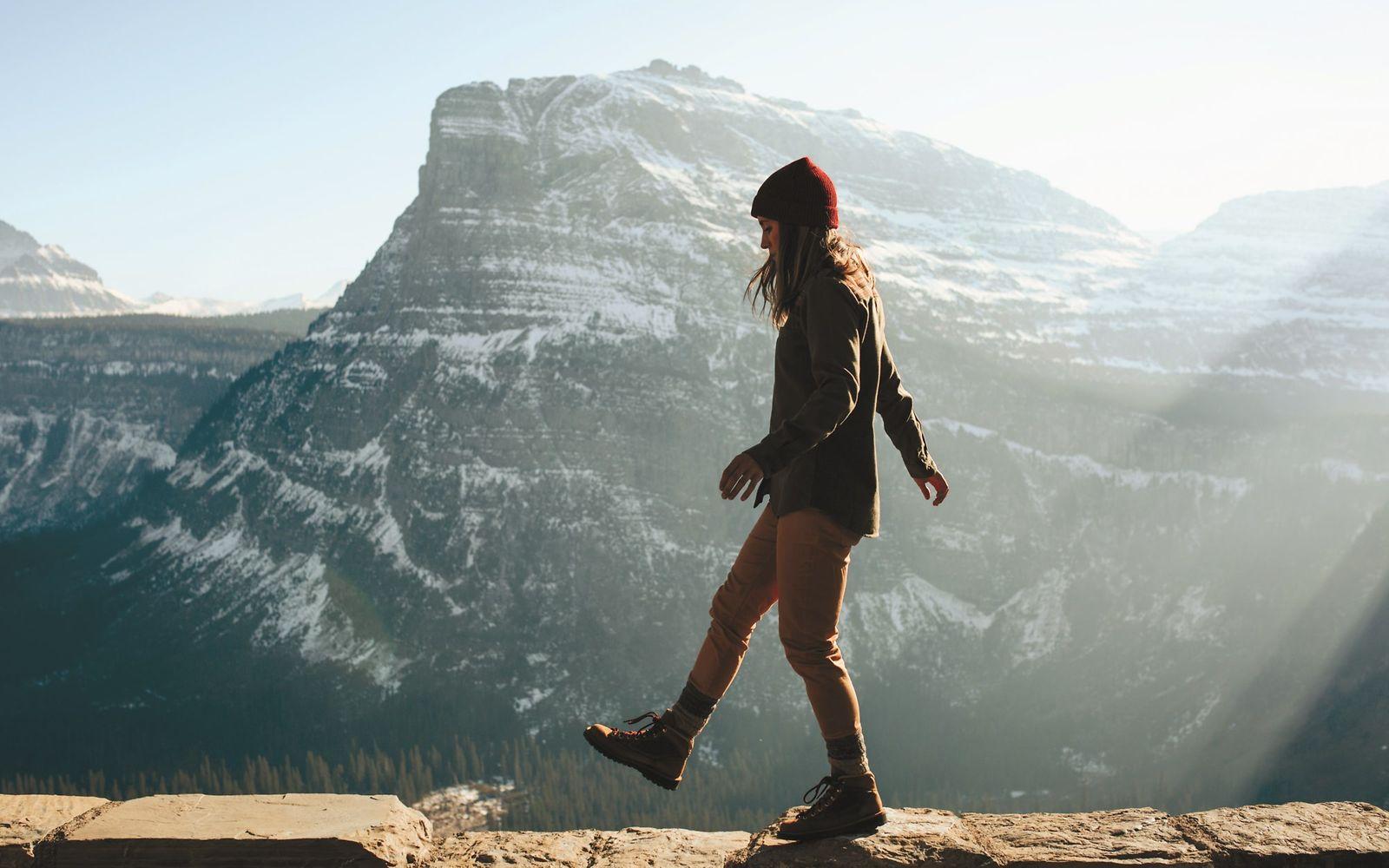 Woman walking on ledge against a beautiful blue mountain range.