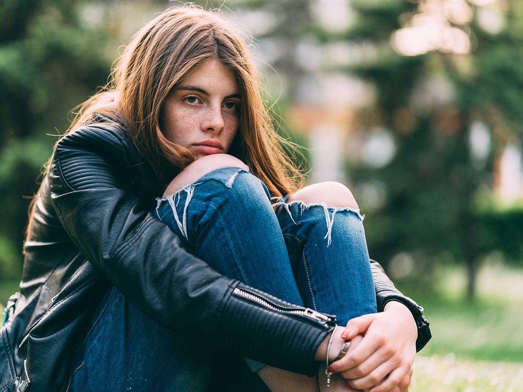 Symbolbild Selbstverletzung Jugendliche: Trauriges Mädchen sitzt im Park