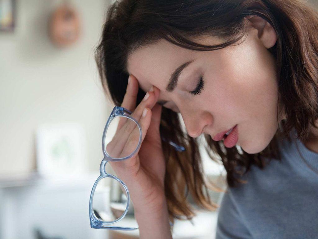 Clusterkopfschmerzen: Frau hält Brille in der Hand und fasst sich an die Stirn.