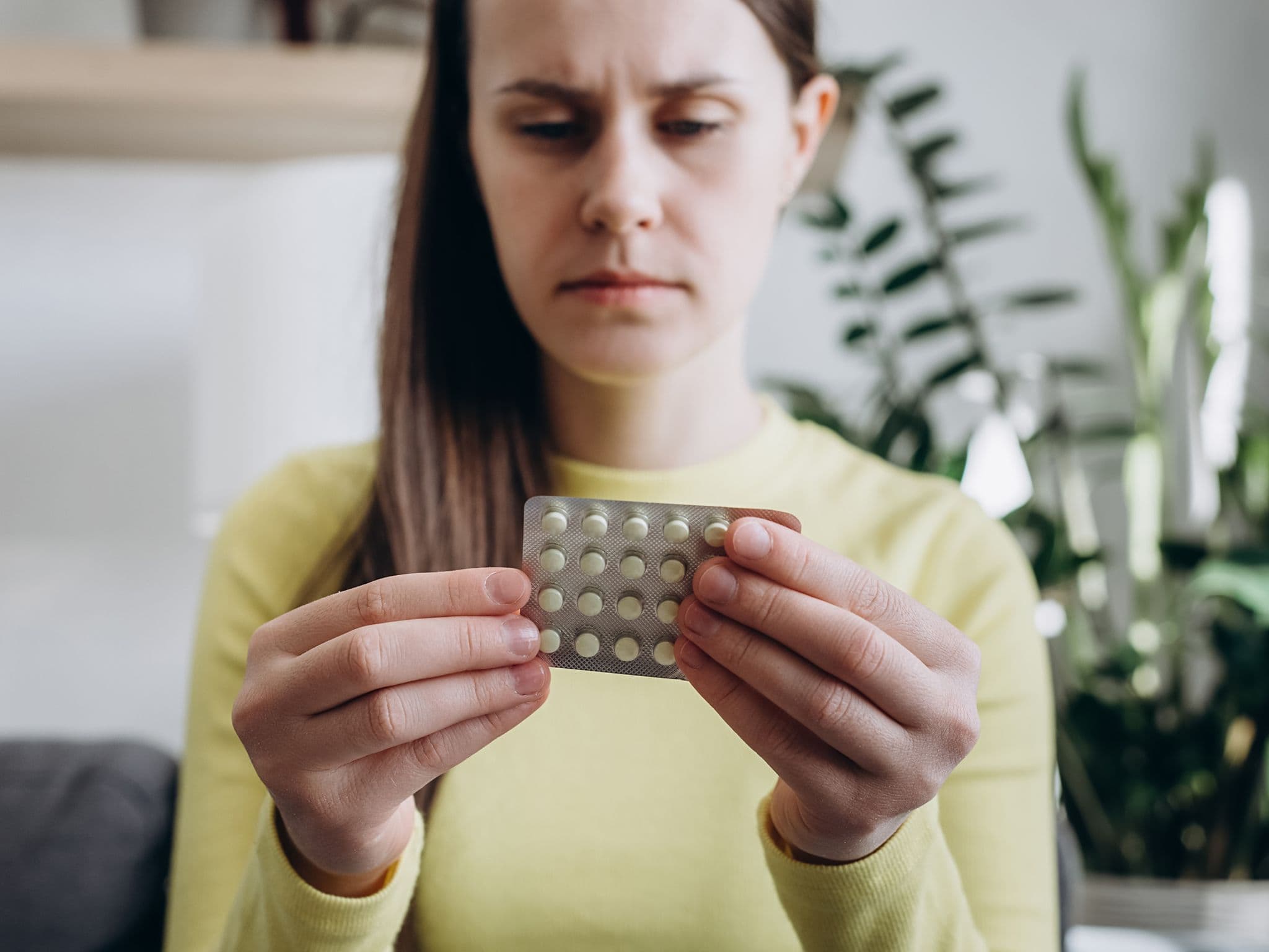 Medikamentensucht: Frau mit Augenringen blickt müde auf eine Packung Tabletten.