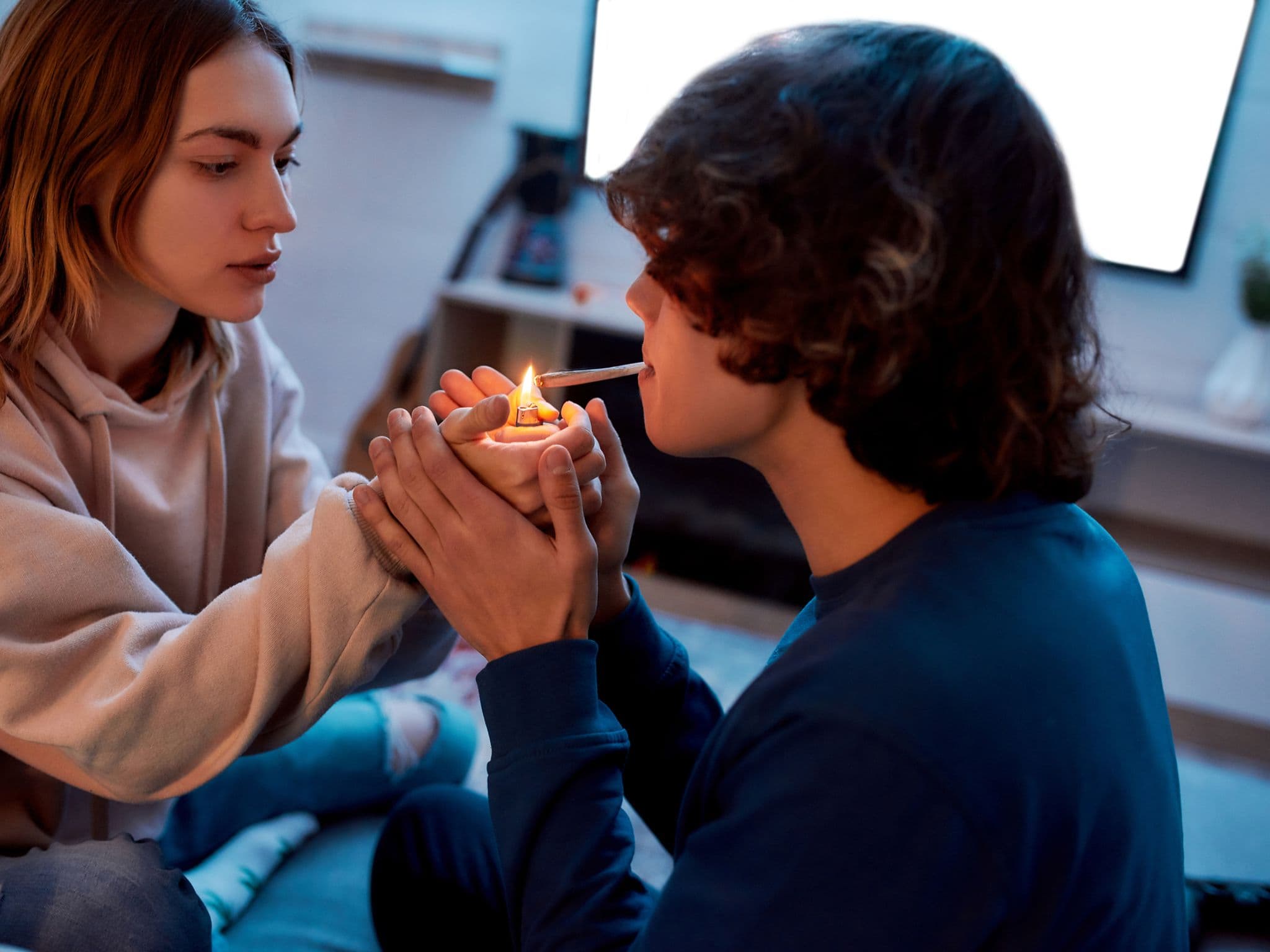 Cannabis: Junges Mädchen, das Cannabis-Zigarette für ihren Freund anzündet, während sie zu Hause auf der Couch sitzt.