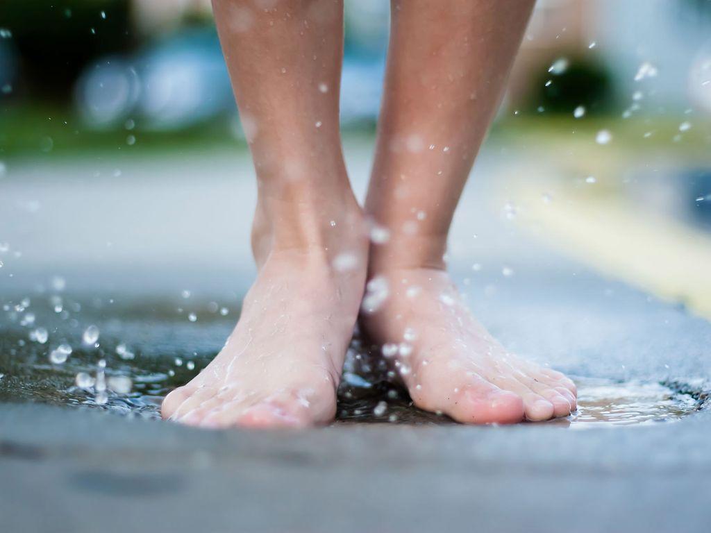 Podologie: Nackte Füße spritzen mit Wasser in einer Pfütze.
