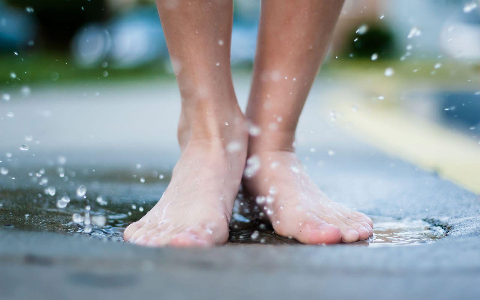 Podologie: Nackte Füße spritzen mit Wasser in einer Pfütze.