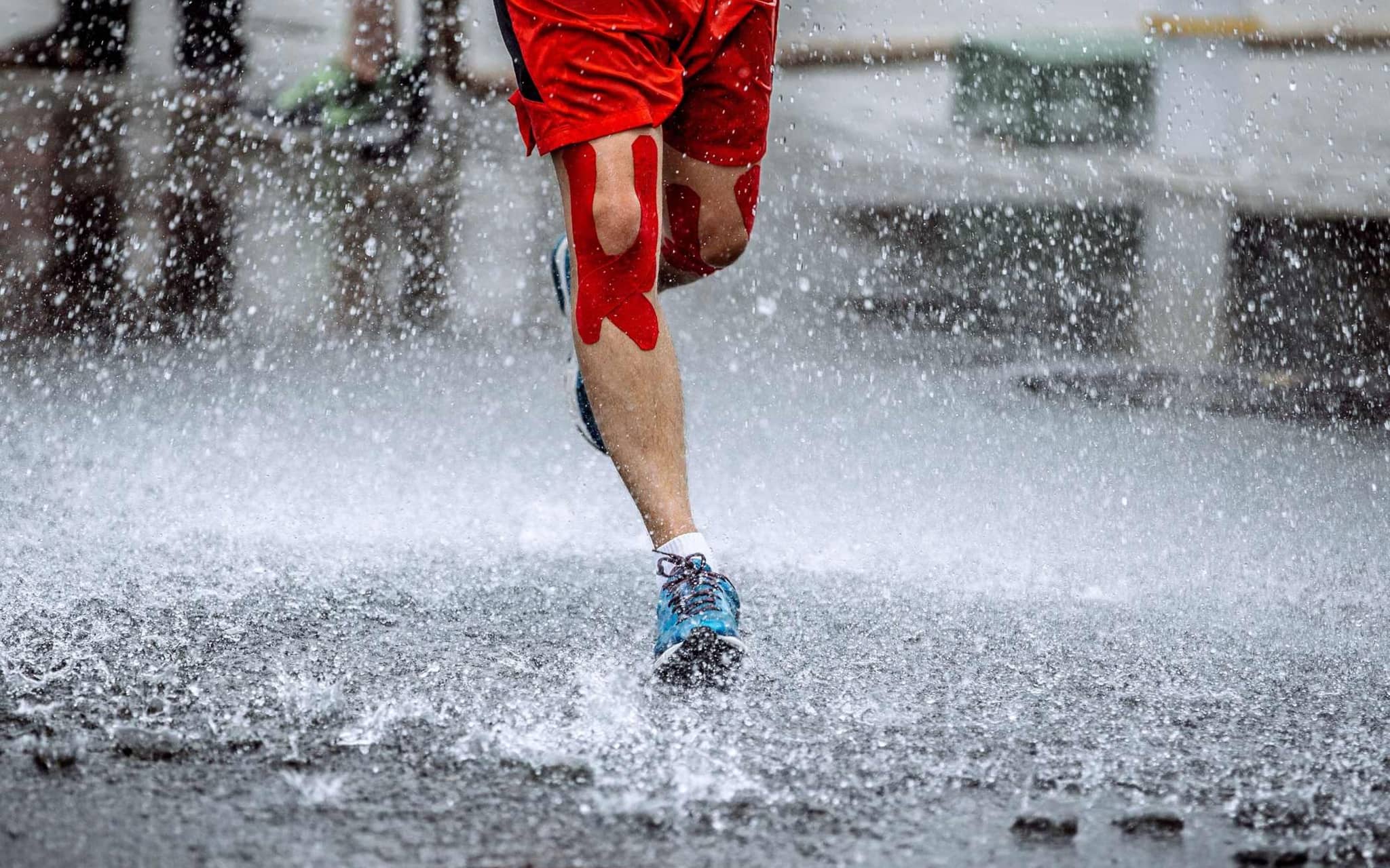 Kinesiotape: Mann mit Kinesiotape am Knie läuft durch Regen.